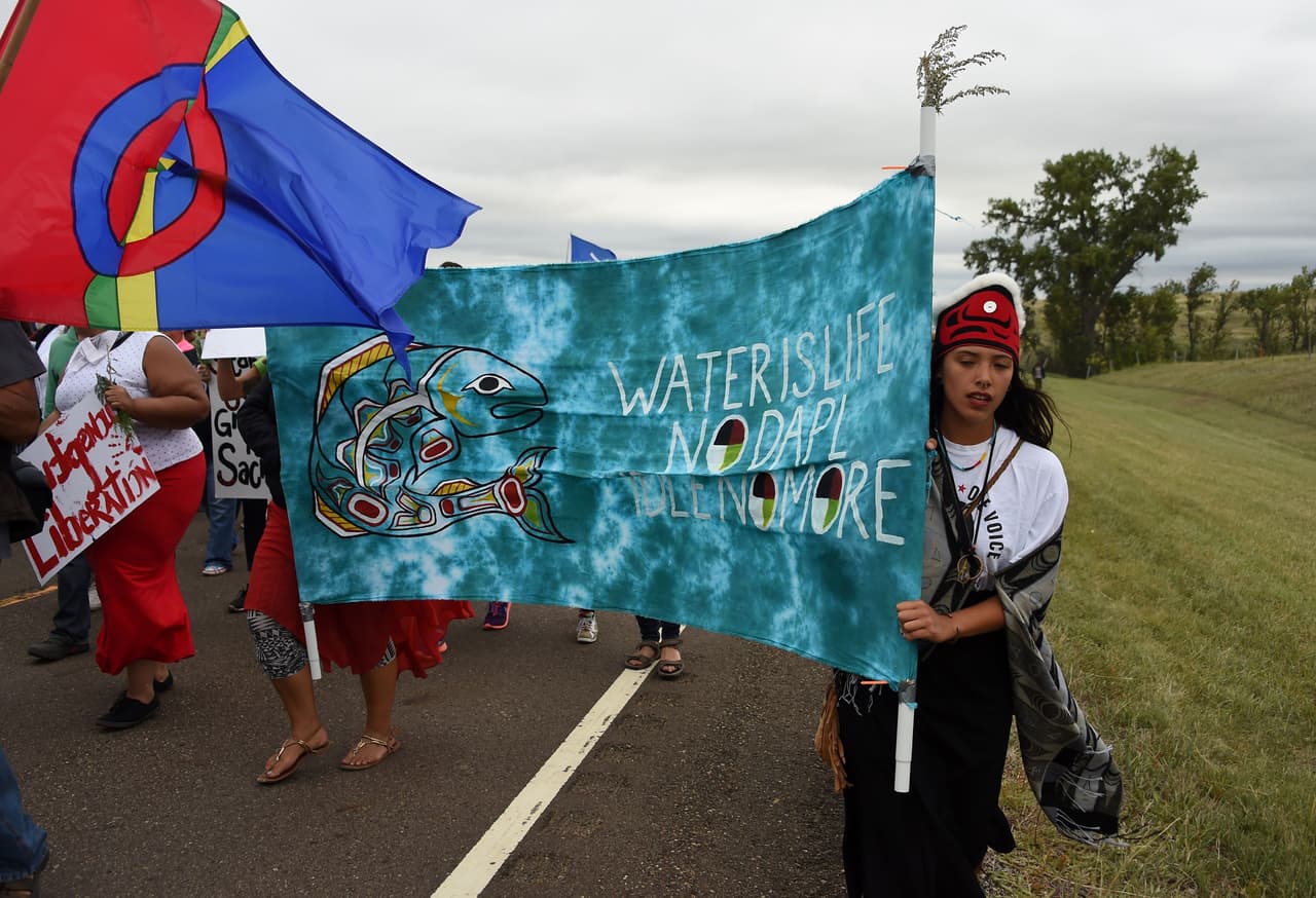 Marcha de indígenas sioux hacia el sitio sagrado dañado por topadoras para construir el oleoducto DAPL. Los activistas, quienes se autodenominan ‘protectores del agua’ llevan un letrero que dice “El agua es vida. No a DAPL. No más petróleo”.