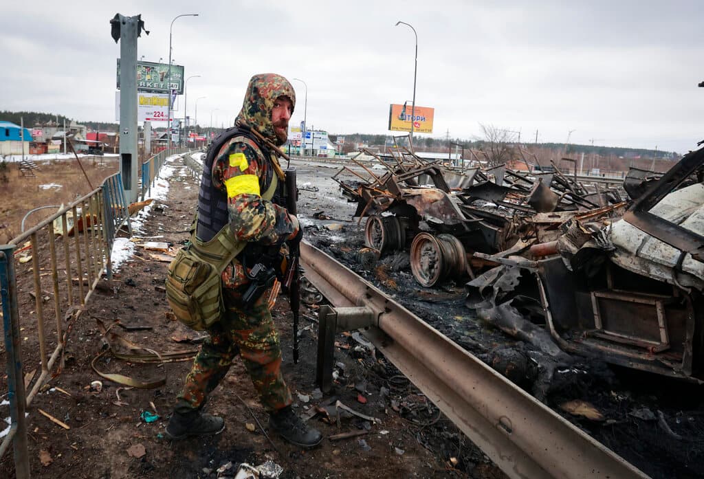 Un hombre armado junto a los restos de un vehículo militar ruso en Bucha, cerca de la capital, Kiev. 
<a href="http://uni.vi/N5YF103rnGs" target="_blank">Un convoy de vehículos blindados y tanques de unas 40 millas de largo</a> y cuya parte frontal se ubica unas 20 millas al norte de la capital ucraniana parece confirmar la teoría del Pentágono de que el Kremlin intenta aislar y sitiar esa ciudad para "decapitar" su gobierno.
