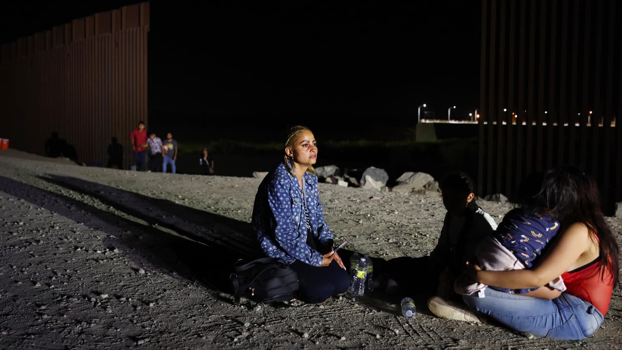 Migrantes que buscan asilo esperan en una estación de agua para presentarse ante un agente de la Patrulla Fronteriza después de cruzar desde México en un espacio a lo largo del muro fronterizo en Yuma, Arizona.