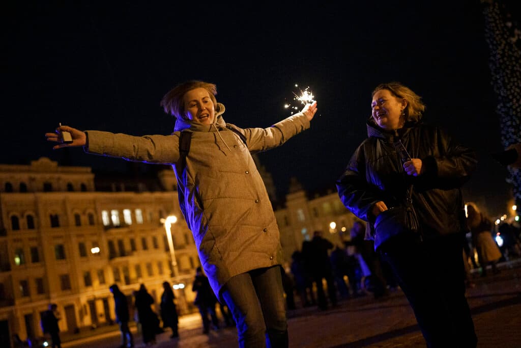Una mujer sostiene una bengala mientras baila en la plaza Sophia antes del toque de queda en la víspera de Año Nuevo en Kyiv, Ucrania, el sábado 31 de diciembre de 2022. Múltiples explosiones sacudieron la capital y otras áreas de Ucrania el sábado.