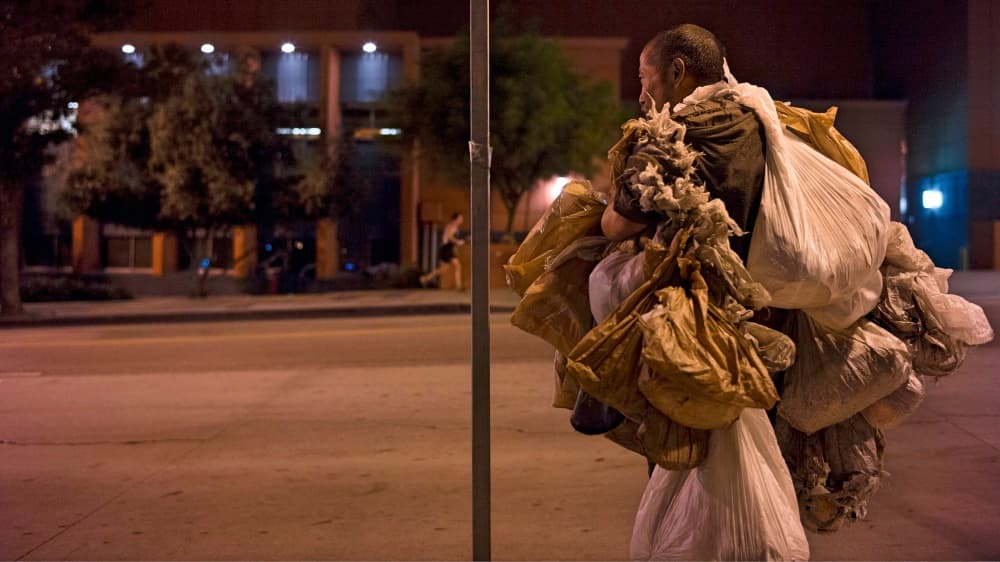 Un indigente de Skid Row camina cargando bolsas de plástico con sus pertencias.