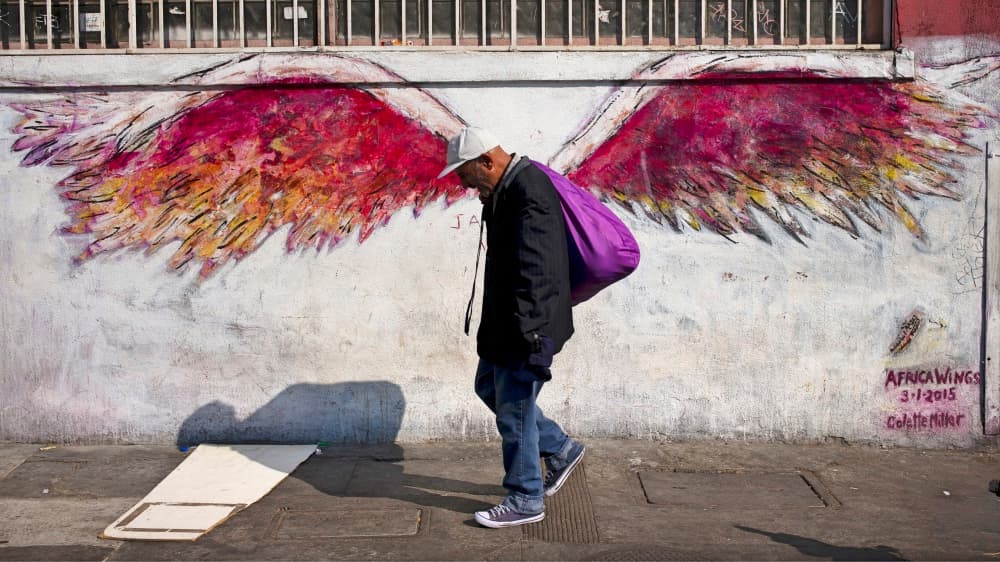 Un hombre pasa frente al mural 'Africa Wings' (alas de África) que pintó la artista Colette Miller en Skid Row tras la muerte de un indigente baleado por agentes del LAPD.