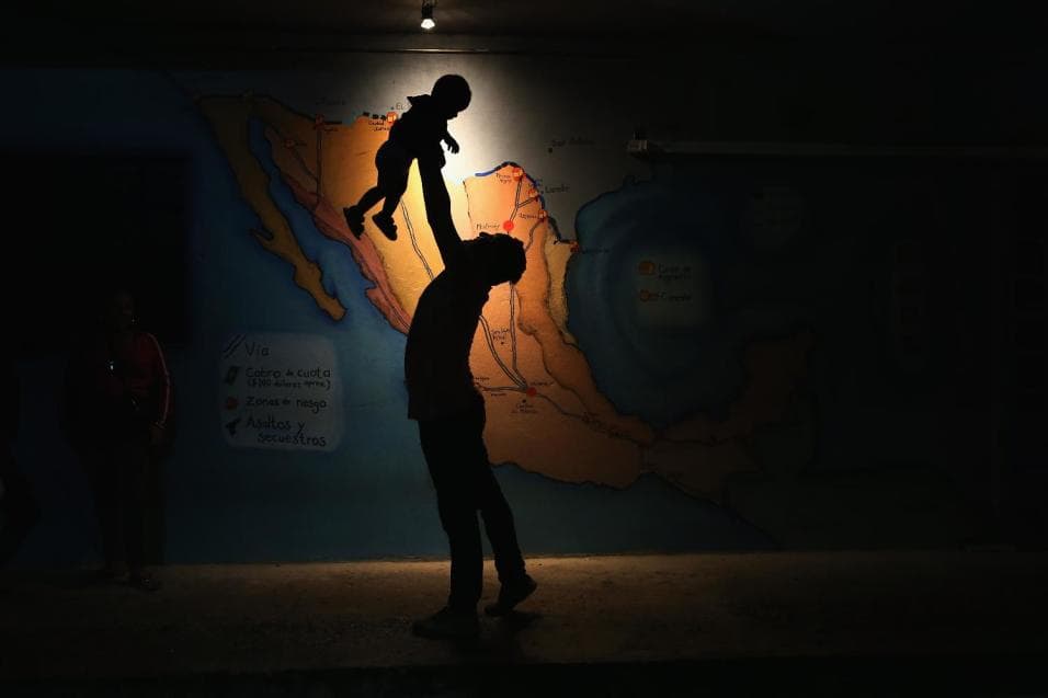 A Honduran migrant plays with a friend's son in front of a Mexico map.