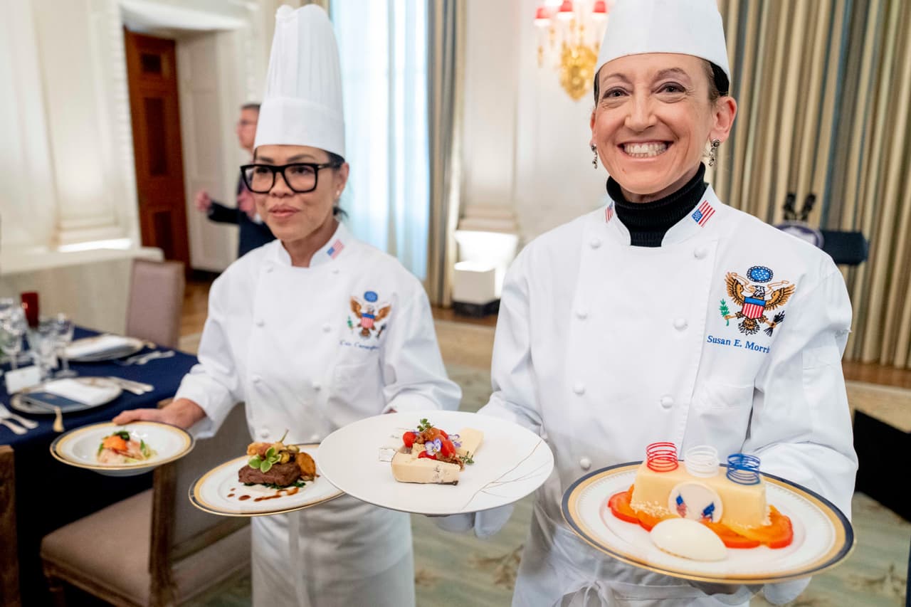 La chef ejecutiva de la Casa Blanca, Cris Comerford, a la izquierda, y la chef pastelera, Susie Morrison, sostienen los platillos del menú. La cena incluyó una langosta de Maine con mantequilla, carne de res con mermelada de chalota, quesos artesanales estadounidenses y bizcocho de naranja con peras asadas y helado de crème fraiche.