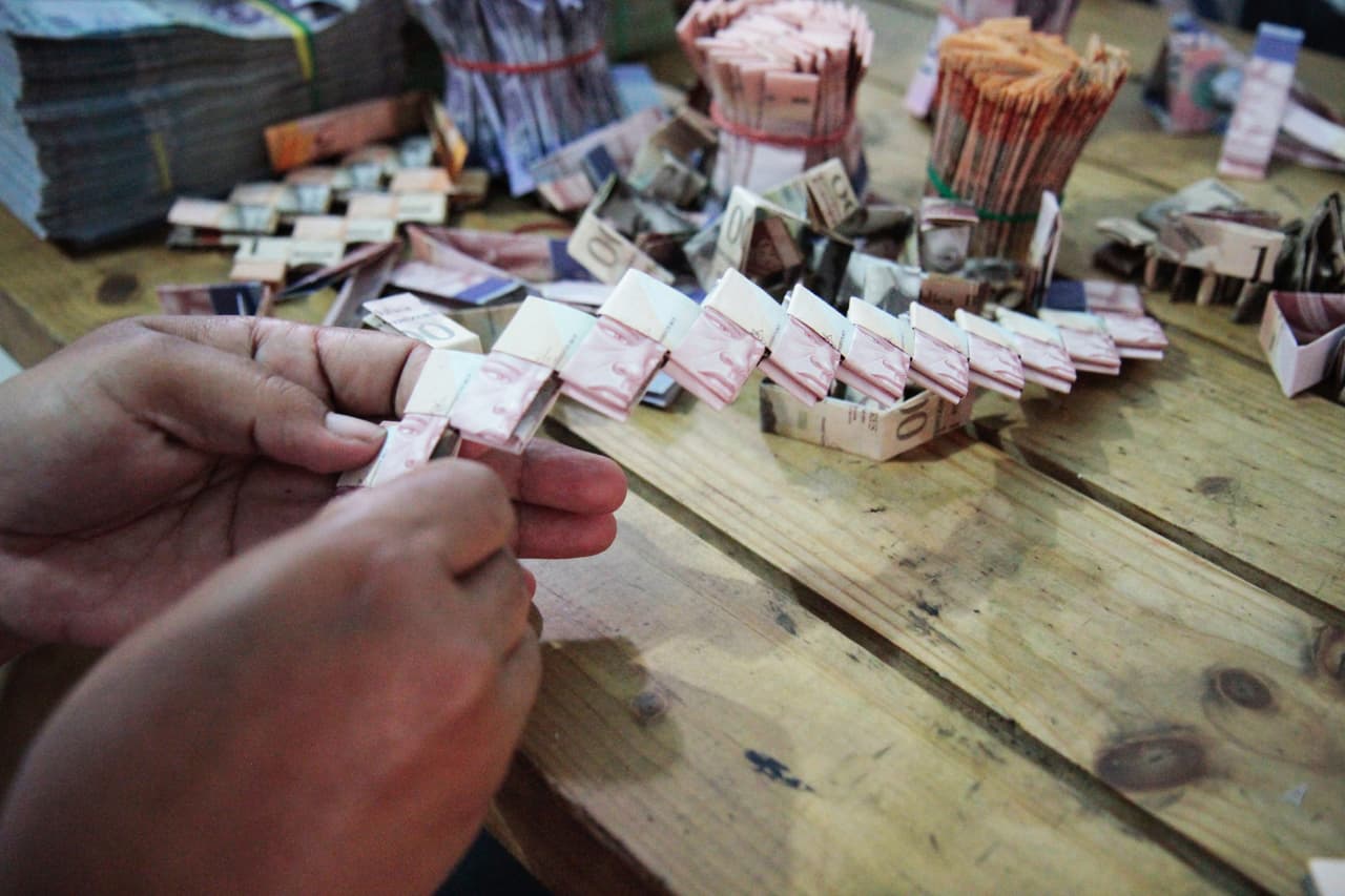 Con la pérdida del valor del dinero, esta pareja de migrantes no dudaron en usar sus bolívares para fabricar artesanías. Para hacer estos bolsos, doblan cientos de billetes en rectángulos y los hilan juntos formando trenzas.