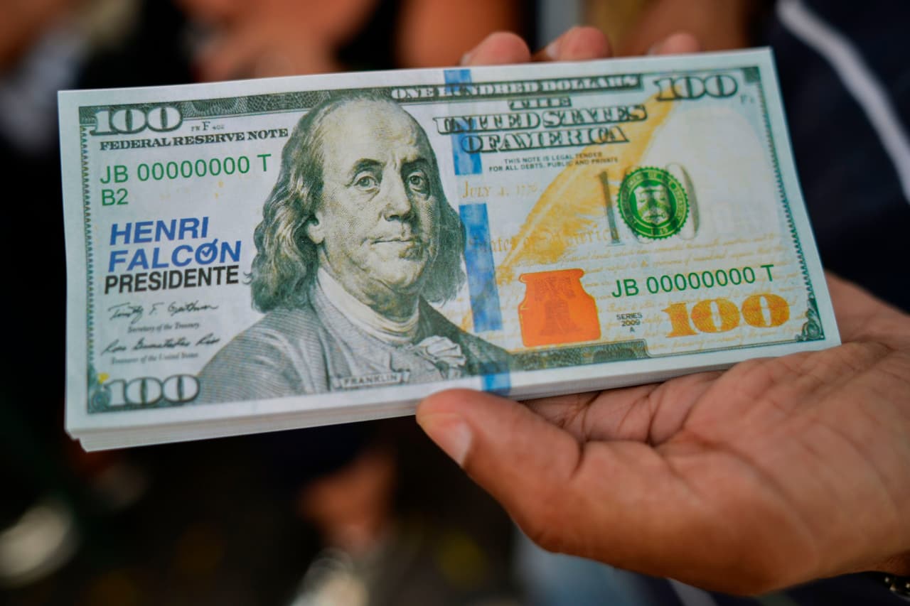 Un hombre sostiene una pieza de propaganda electoral de la campaña de Henri Falcón, que simula un billete de cien dólares.