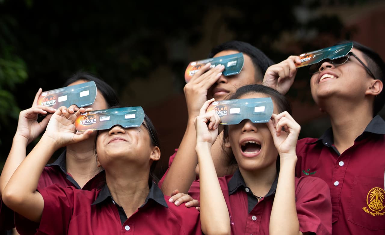 Estudiantes usan filtros especiales para visualizar el eclipse solar desde su escuela en Bangkok, Tailandia.