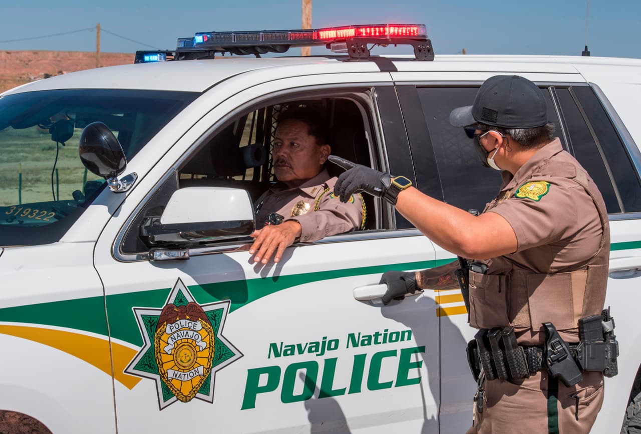 Los oficiales de policía de la Nación Navajo manejan un punto de control durante el toque de queda de 57 horas impuesto para tratar de detener la propagación del coronavirus. Aunque la mayoría de los residente viven de la minería, hoteles y casinos, como muchas otras reservas indígenas, los navajos también sufren un elevado índice de pobreza, abuso de sustancias, violencia sexual, bajos niveles de educación, desempleo, servicios de salud deficientes y viviendas precarias. Según varios estudios, si se considera un estado serían el más pobre de todo EEUU.