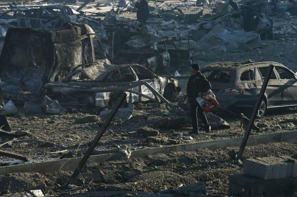 Un hombre camina con su perro por 
<b>los destrozos de vehículos y edificios que dejó el bombardeo</b>. Los vecinos de la zona se han acercado al área y han contado a los periodistas cómo han vivido el ataque. Los rusos "probablemente apuntaban a una central (eléctrica) térmica a unos cientos de metros", dijo Vladimir, de 76 años, a la agencia 
<i>AFP</i> señalando una gran chimenea blanca en el horizonte.
<br>