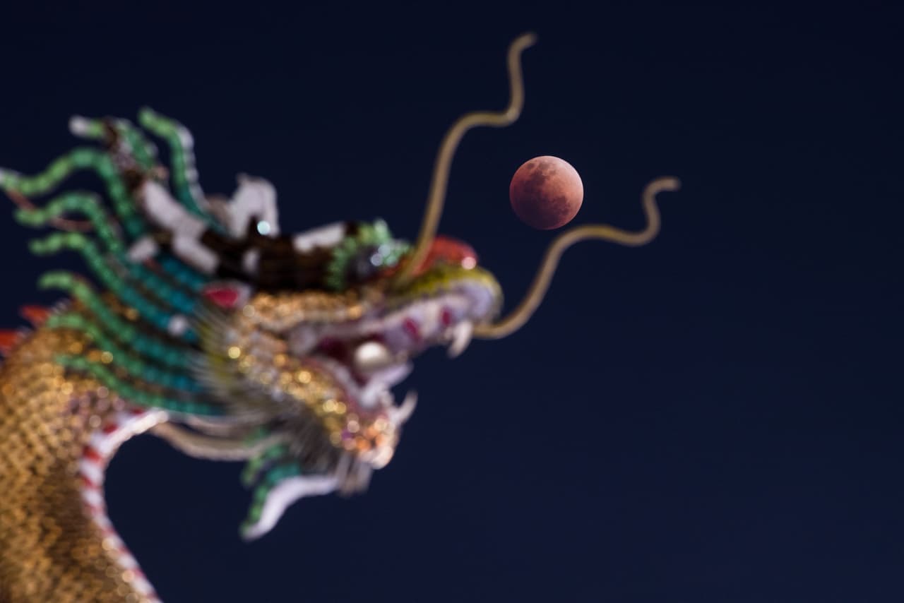 La luna roja y la estatua de un dragón chino en un templo budista. Bangkok, Tailandia.