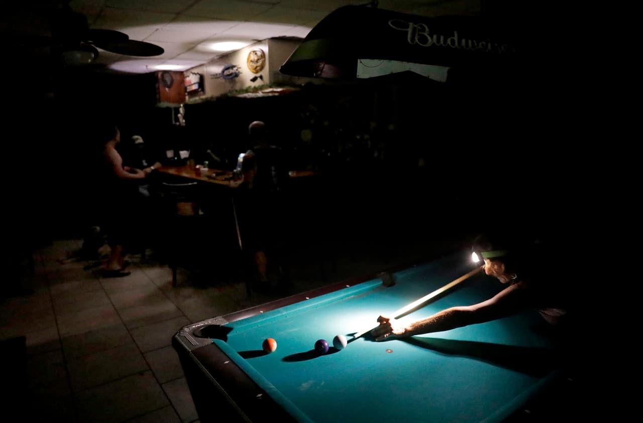 La falta de luz no impide que gente como Lisa Borruso jueguen al billar usando una linterna en su frente en Gators Crossroads en Naples.