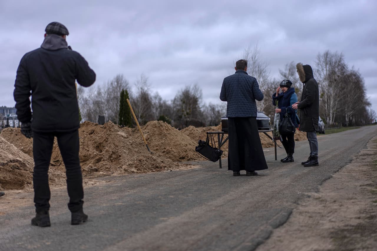 Vlad Minchenko, a la izquierda, observa cómo Natalya Verbova, de 49 años, y su hijo Roman Verbovyi, de 23, asisten al funeral de su esposo Andriy Verbovyi, de 55, quien fue asesinado por soldados rusos mientras servía en la defensa territorial de Bucha, en las afueras de Kiev, Ucrania, el 13 de abril de 2022. Minchenko, que antes se dedicaba a hacer tatuajes, ahora entierra a las personas que recupera los cuerpos de los muertos 
<a href="https://www.univision.com/noticias/mundo/guerra-ucrania-rusia-ultimas-noticias-en-vivo-nueva-ofensiva-18-de-abril" target="_blank">por la guerra en Ucrania</a>.