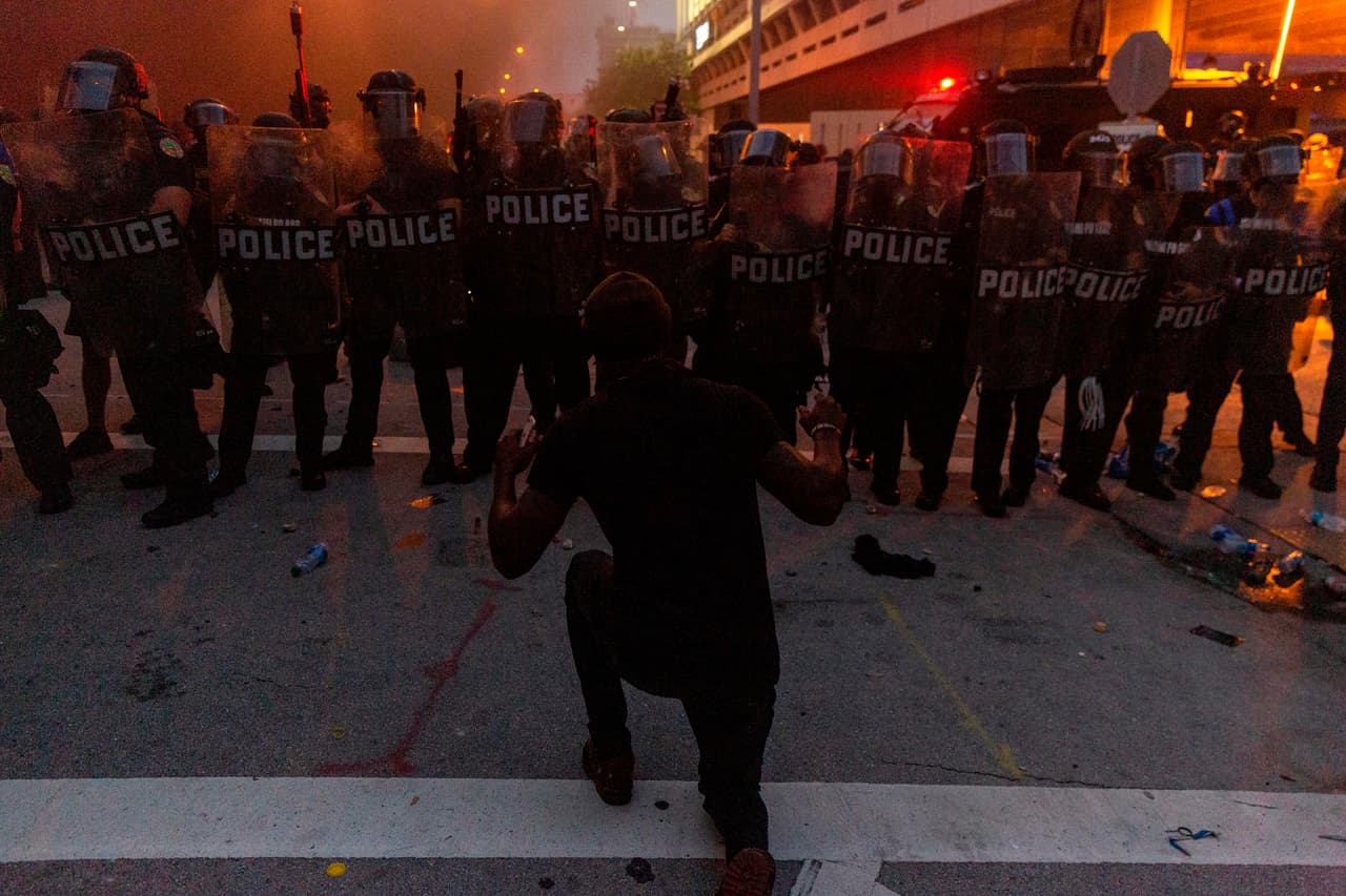 A protestor kneels and raises his hand in front of a line of riot police during a protest against police brutality in Miami, Florida on May 30, 2020 in response to the recent death of George Floyd, an unarmed black man who died while while being arrested and pinned to the ground by the knee of a Minneapolis police officer. - Demonstrations are being held across the US after George Floyd died in police custody on May 25. (Photo by Adam DelGiudice / AFP) (Photo by ADAM DELGIUDICE/AFP via Getty Images)