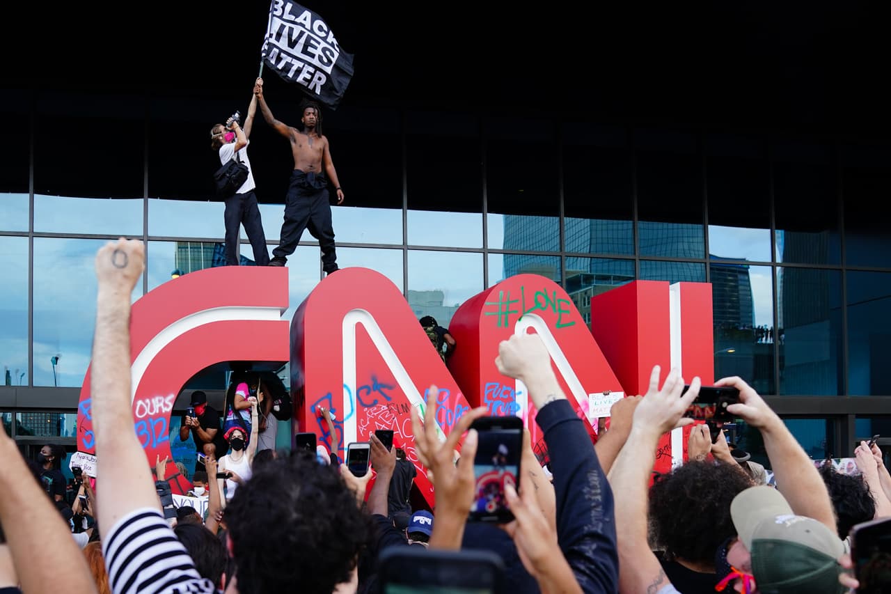Un hombre agita una bandera de Black Lives Matter sobre el emblema CNN durante una protesta en respuesta al asesinato policial de George Floyd frente al Centro CNN el 29 de mayo de 2020 en Atlanta, Georgia.