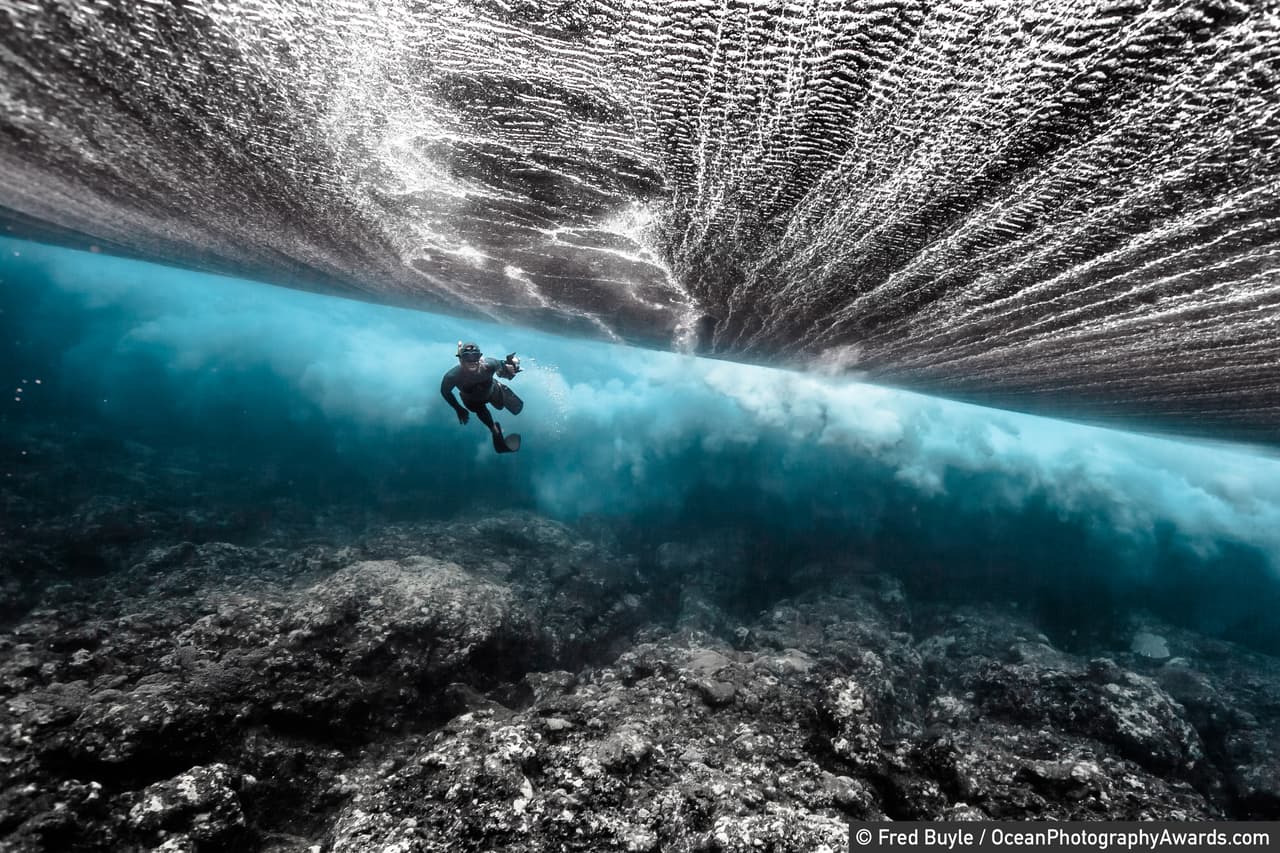 <b>Un buzo nada bajo de una ola que rompe cerca de la orilla.</b> La foto fue tomada en la la isla de Rurutu, Polinesia Francesa, y fue finalista en la categoria ‘exploración’. 
<br>